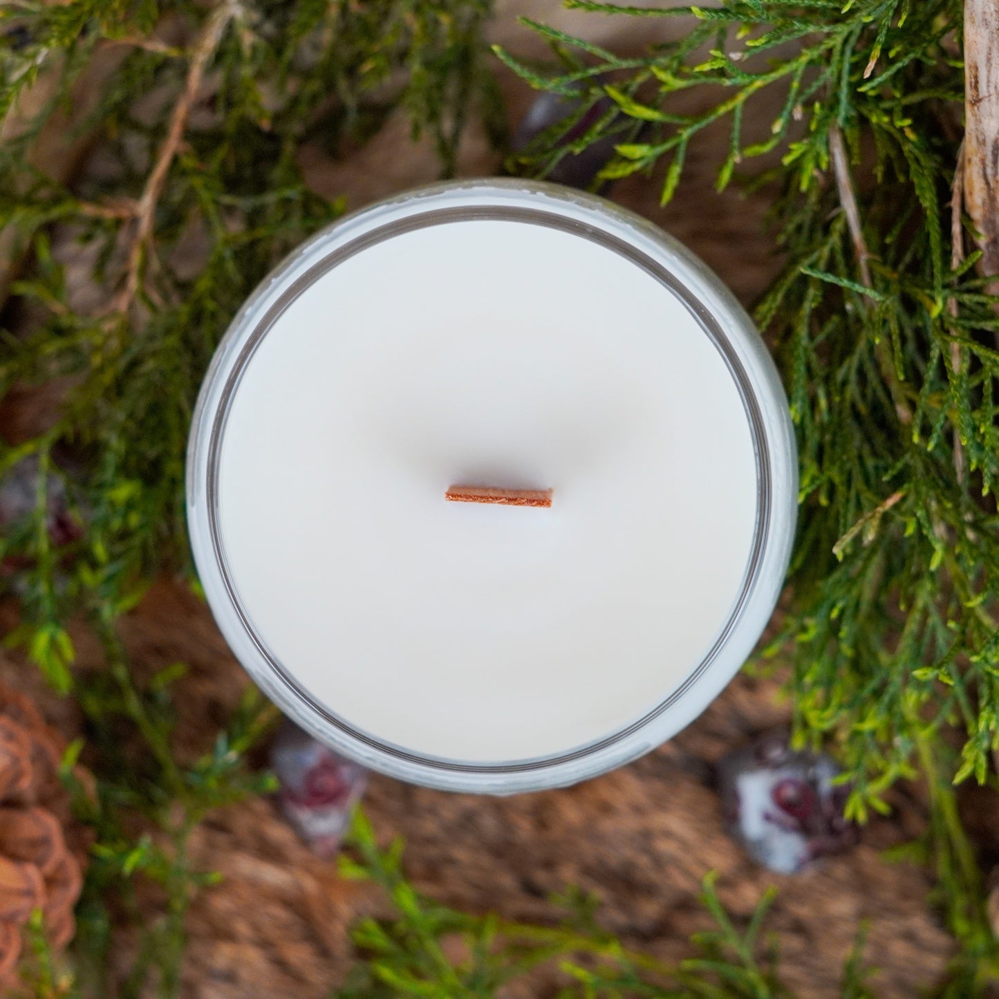 Top-down view of the "Barbarian" soy candle with a single wooden wick in the center. The wax is smooth and unburned, and the candle is surrounded by natural elements like pine, wood, and dice.
