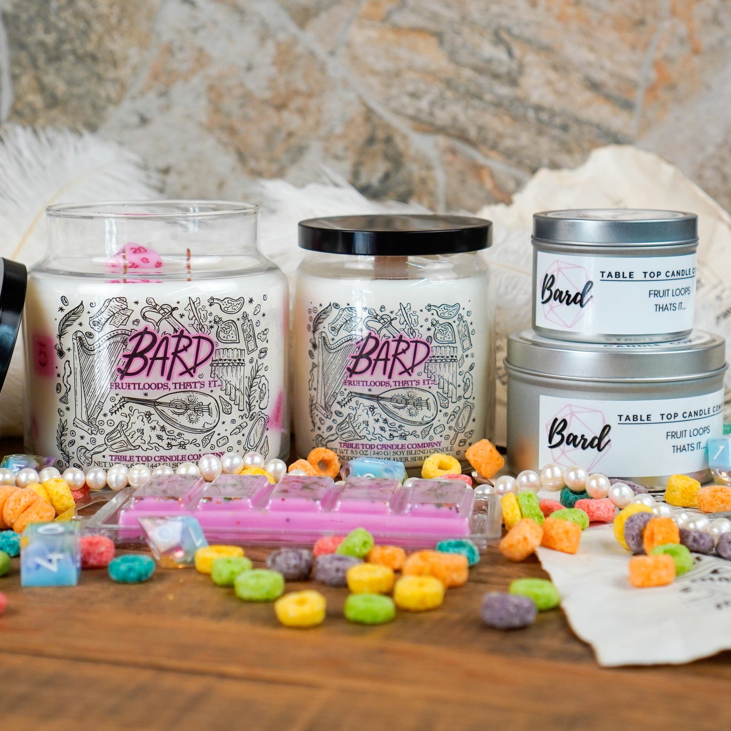 A full product lineup of the "Bard" candle collection by Table Top Candle Company. Includes large and small jar candles, tins, and wax melts, all scented like fruit loops. Surrounded by colorful cereal, pearls, and fantasy dice.